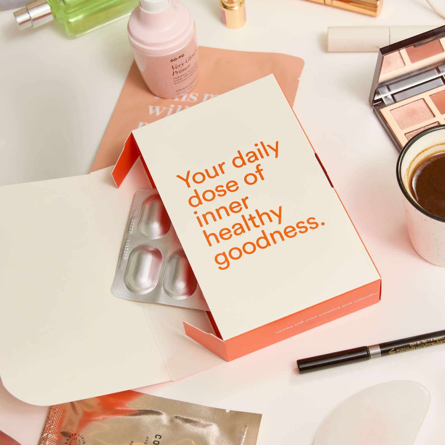 Product packaging with text 'Your daily dose of inner healthy goodness' on a table with various makeup items.
